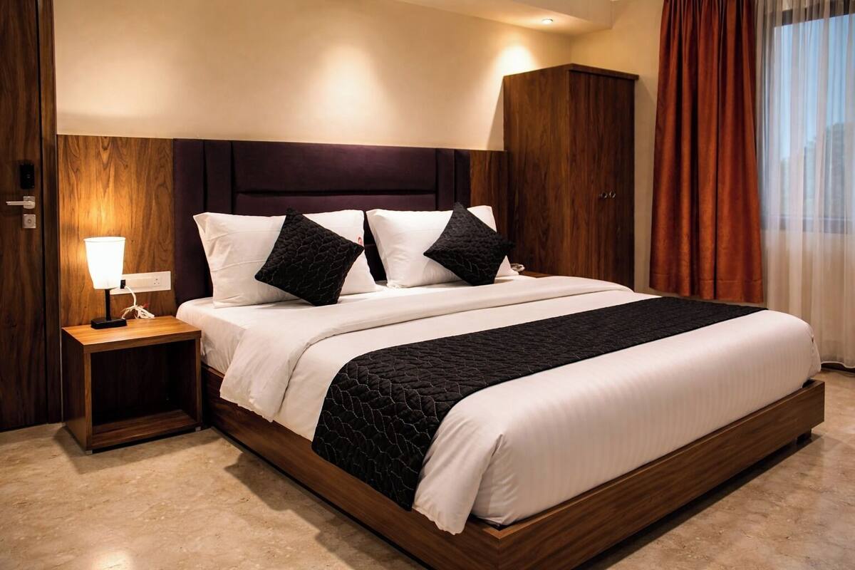 A hotel room with a large bed, a nightstand with a lamp, wooden headboard, and a wardrobe.