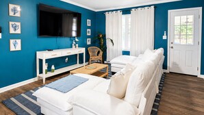 Ein Wohnzimmer mit einem weißen Sofa, einem Fernseher, einem Deckenventilator und einer Tür.