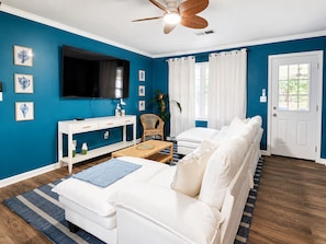 A living room with a white sofa, a TV, a ceiling fan, and a door. - 4BR Coastal Look, Pool House, Pets welcome (Columbus)