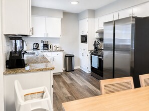 A modern kitchen with white cabinets, a stainless steel refrigerator, a coffee maker, and a blender. - 4BR Coastal Look, Pool House, Pets welcome (Columbus)