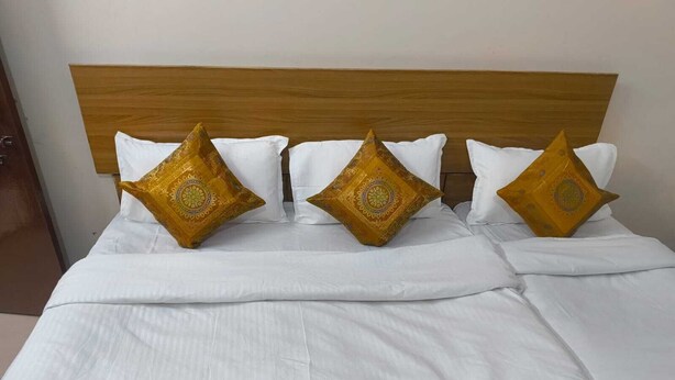 Una cama con cabecera de madera, ropa de cama blanca y almohadas doradas decorativas.
