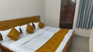 Una cama con ropa de cama blanca, un edredón estampado, cabecera de madera y almohadas decorativas.