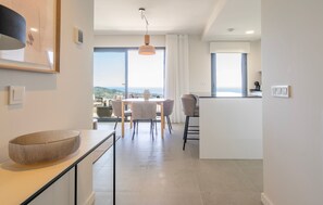 A modern kitchen with a large island, a dining area with a view, and a spacious living area with a large window. - Modern Costa Living: Sleek Three-Bedroom Apartment with Shared Pool & Fitness Center (Rincón de la Victoria)