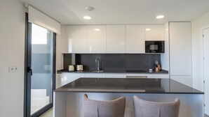 Een moderne keuken met een centraal eiland, twee barkrukken en een magnetron erboven.