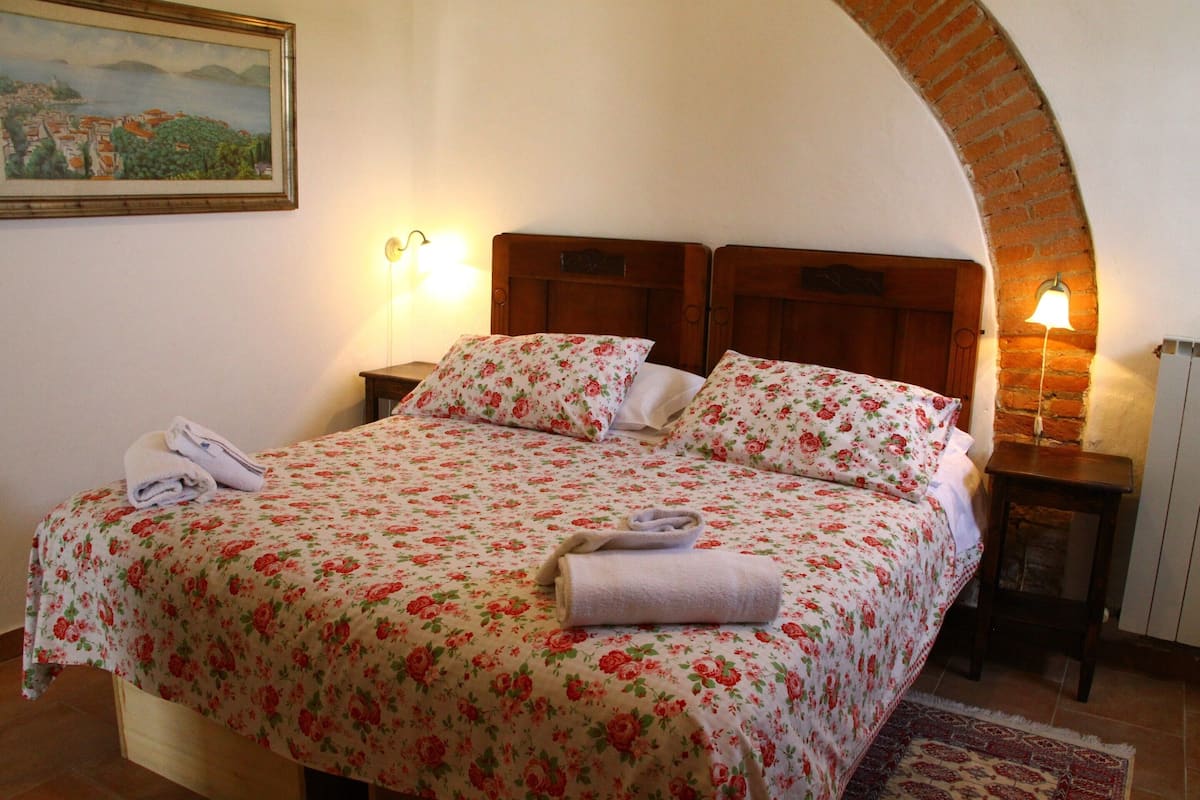 A bed with floral bedding, a towel, and a painting on the wall.