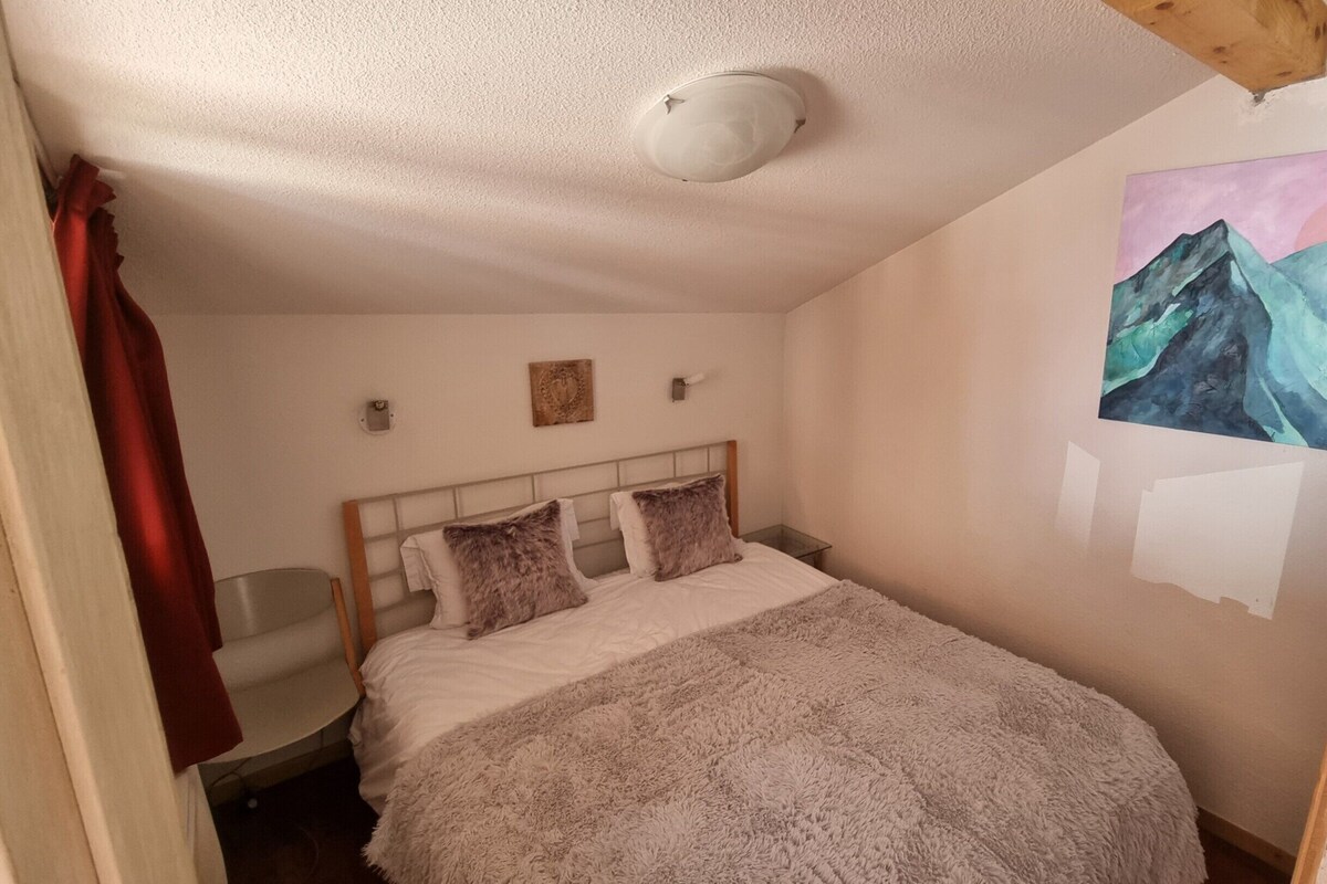 A bedroom with a bed, a ceiling light, a painting, and a red curtain.