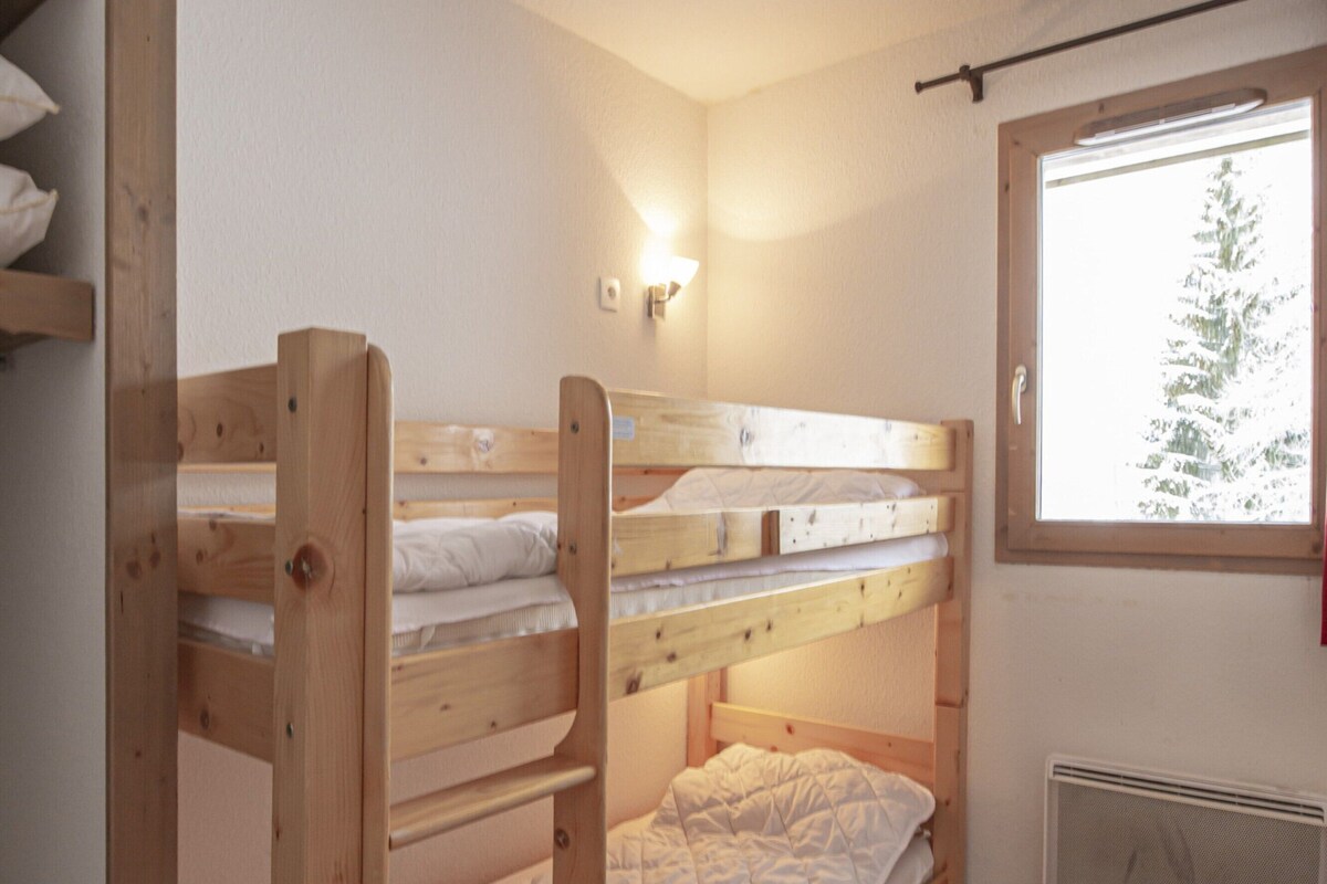 A bunk bed room with a window, wooden flooring, and a wall-mounted heater.