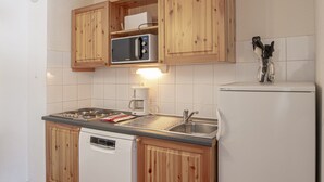A compact kitchen with wooden cabinets, a microwave, a coffee maker, and a dishwasher. - Apartment in Valfrejus Near Gondola (Modane)