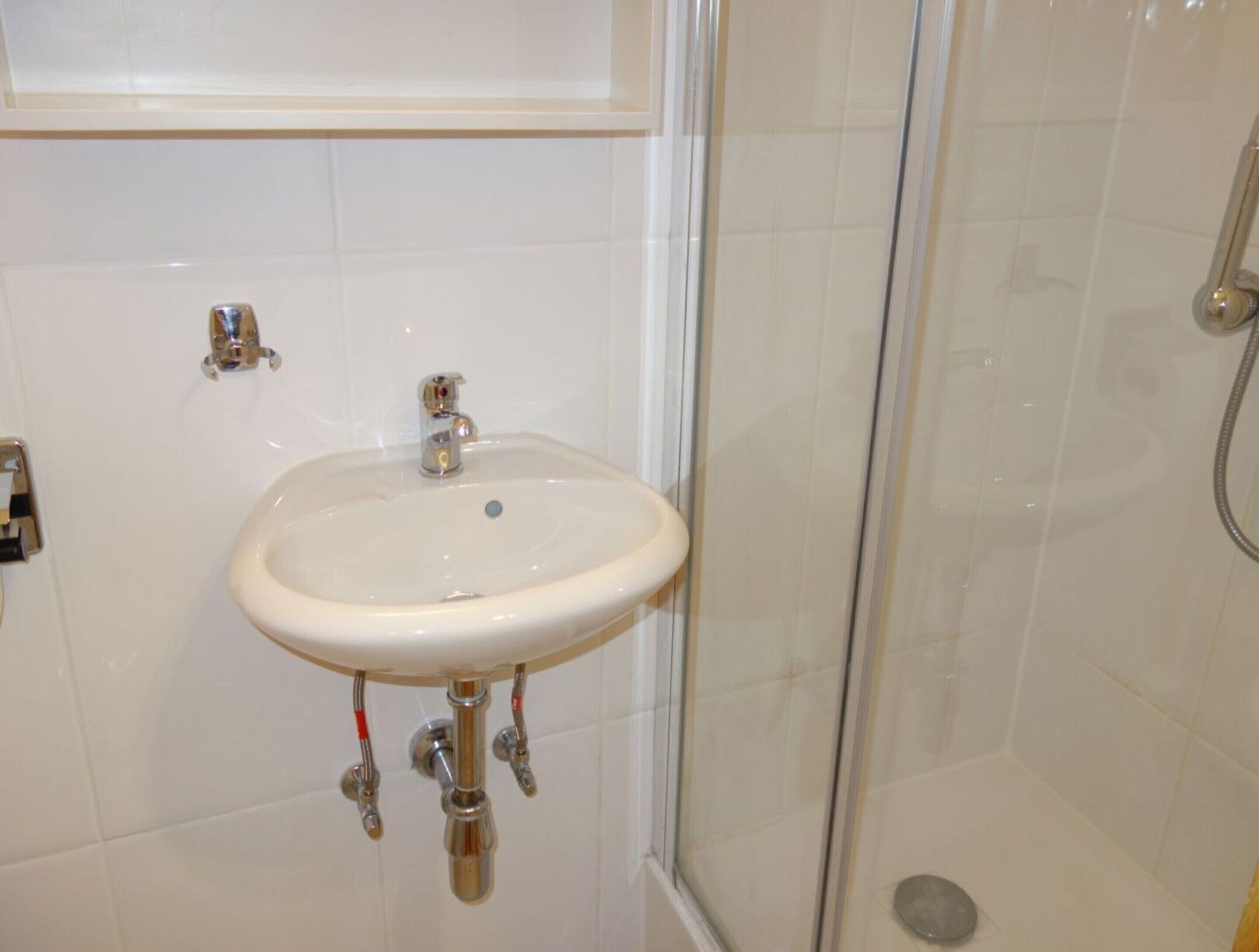 A bathroom with a white sink, a glass shower enclosure, and white tiled walls.
