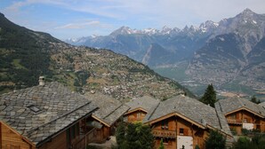A mountain village with traditional wooden houses, a valley, and snow-capped mountains in the background. - Cozy Apartment for Groups (Sion)