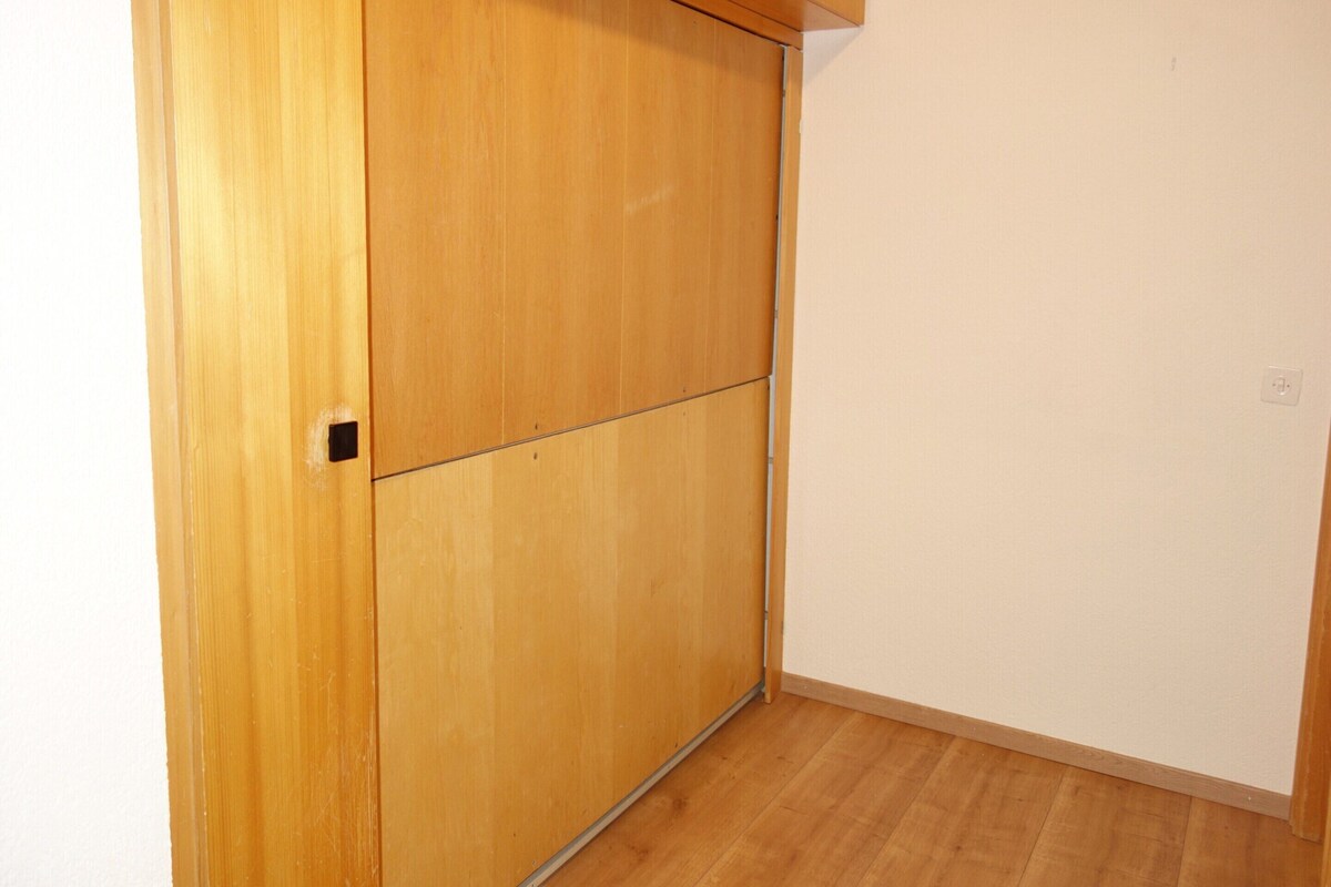 A room with a wooden wardrobe, a wooden floor, and a white wall.