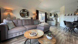 A modern living room with a grey sofa, two round wooden tables, and a kitchen in the background. - Home in the Historic Sint Nicolaasga (Sint Nicolaasga)