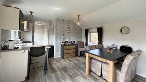 A compact kitchen with a dining area, wooden flooring, and a small window with curtains. - Home in the Historic Sint Nicolaasga (Sint Nicolaasga)