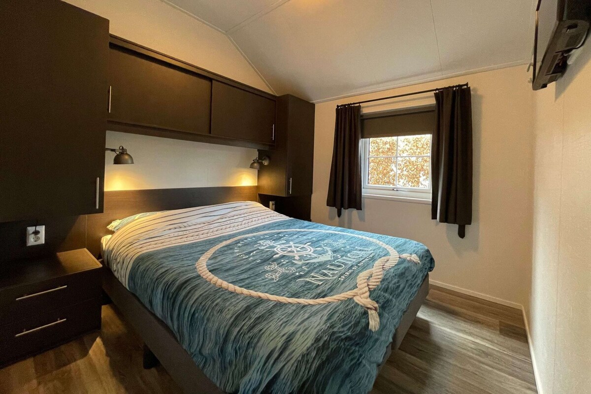 A bedroom with a bed, dark wooden wardrobe, bedside lamps, a window with curtains, and a ceiling light.
