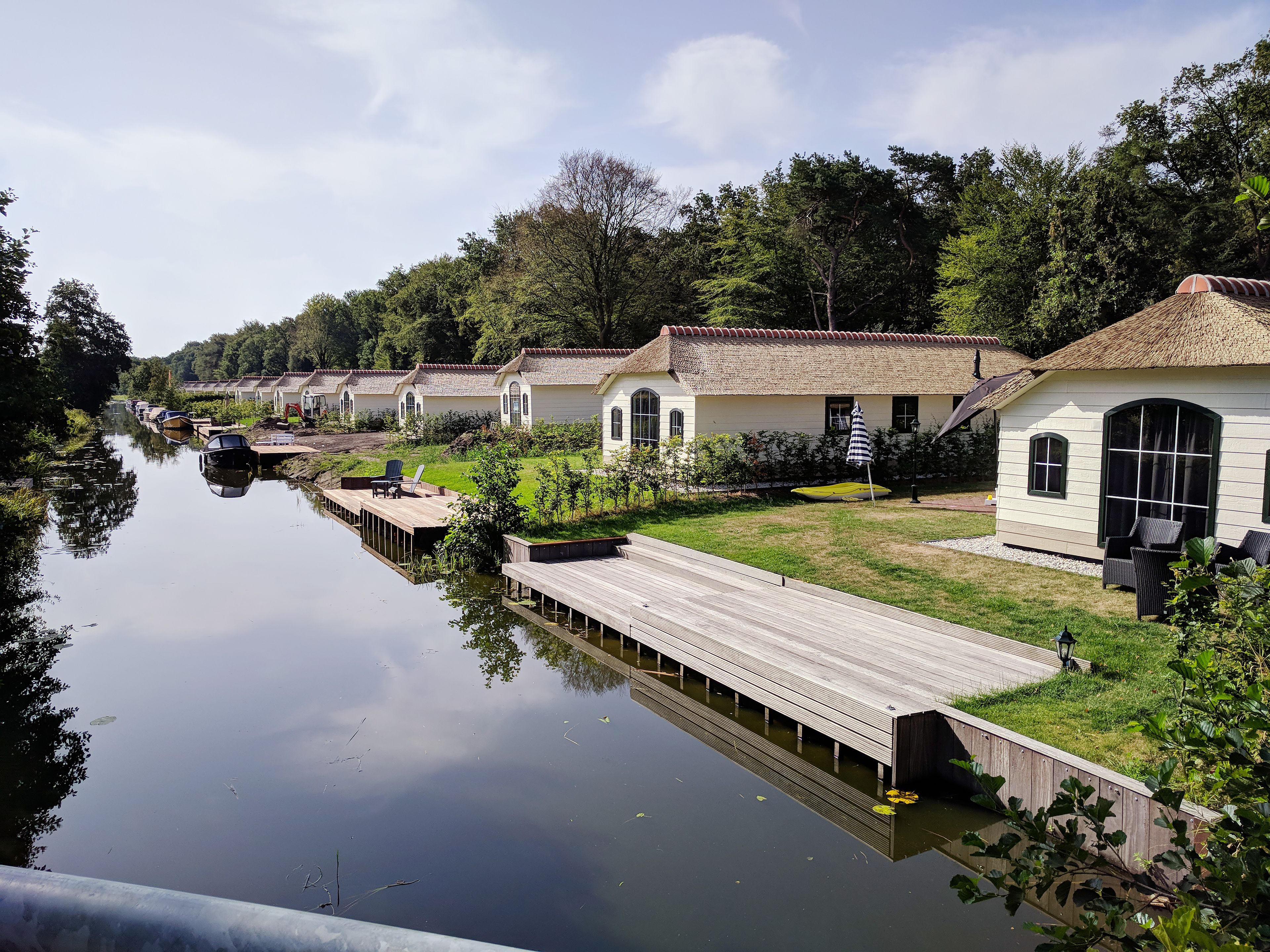 A row of white cottages with thatched roofs along a calm river, connected by wooden walkways.