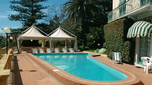 Une piscine avec des chaises longues, un belvédère et un espace salon abrité.