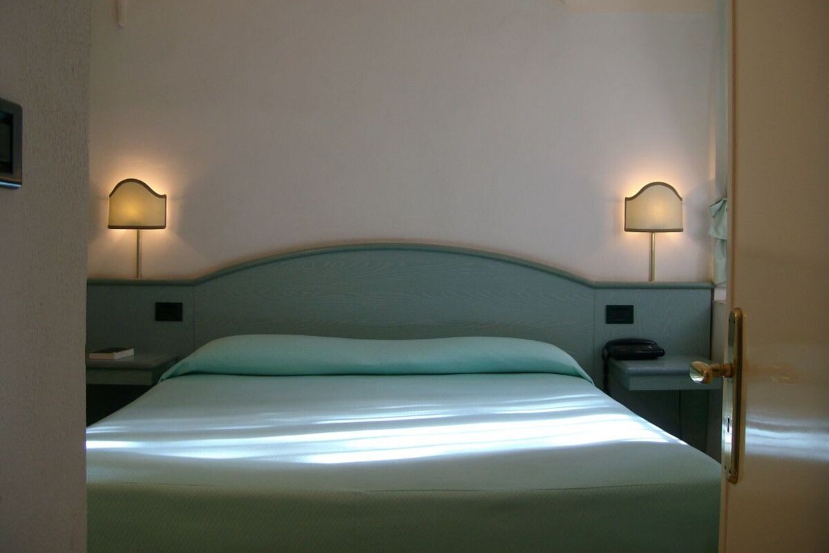 Ein Hotelzimmer mit einem Bett, zwei Nachttischlampen, einem Nachttisch und einer Tür.