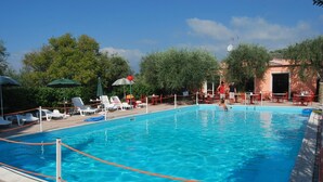 A rectangular swimming pool with clear blue water, surrounded by lounge chairs and umbrellas, and a building with a red roof in the background. - Ferienwohnung fur 4 Personen in Imperia (Imperia)