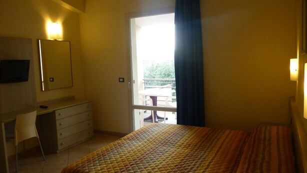 A bedroom with a bed, a desk, a chair, a TV, a window with curtains, and a balcony view. - Ferienwohnung fur 4 Personen in Imperia (Imperia)