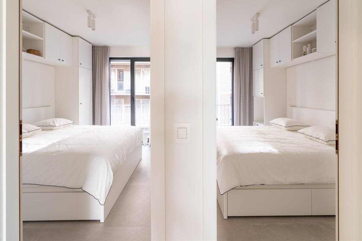 Une vue en miroir d’une chambre d’hôtel avec deux lits, des armoires intégrées et une vue sur l’extérieur.
