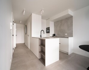 A modern kitchen with white cabinetry, a central island with a sink, and a grey backsplash. - Penthouse in Blankenberge Near the Beach (Blankenberge)