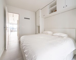Une chambre à coucher au style minimaliste, avec un grand lit, des murs blancs et des rangements intégrés.