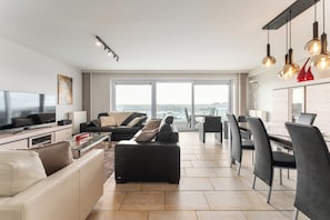 Un salon moderne comprenant un canapé, une table basse, un téléviseur et un coin repas avec des chaises et une table.