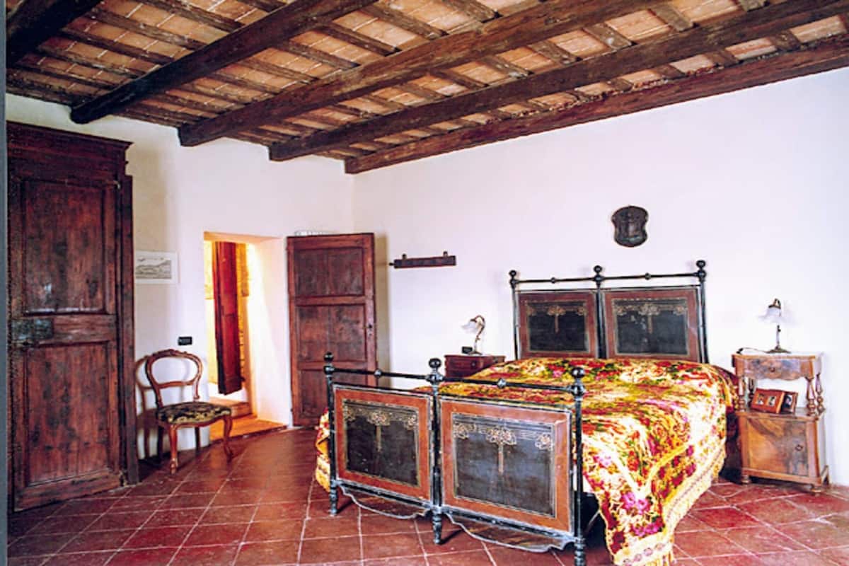 Une pièce avec un lit en bois, une chaise, une armoire en bois et un sol carrelé.