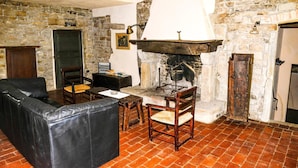 A room with a stone wall, a fireplace, a leather sofa, and a wooden table. - Farmhouse in Modigliana With Scenic Views (Modigliana)