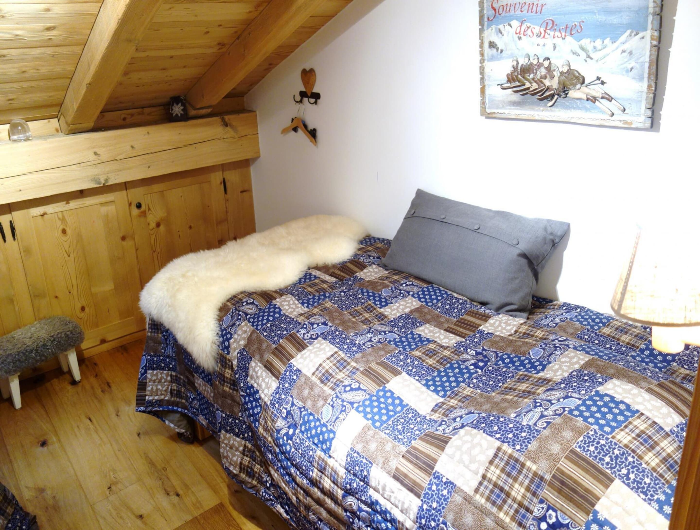 Een slaapkamer met een houten plafond, een geborduurde spreidekbed, een grijs kussen en een poster aan de muur.