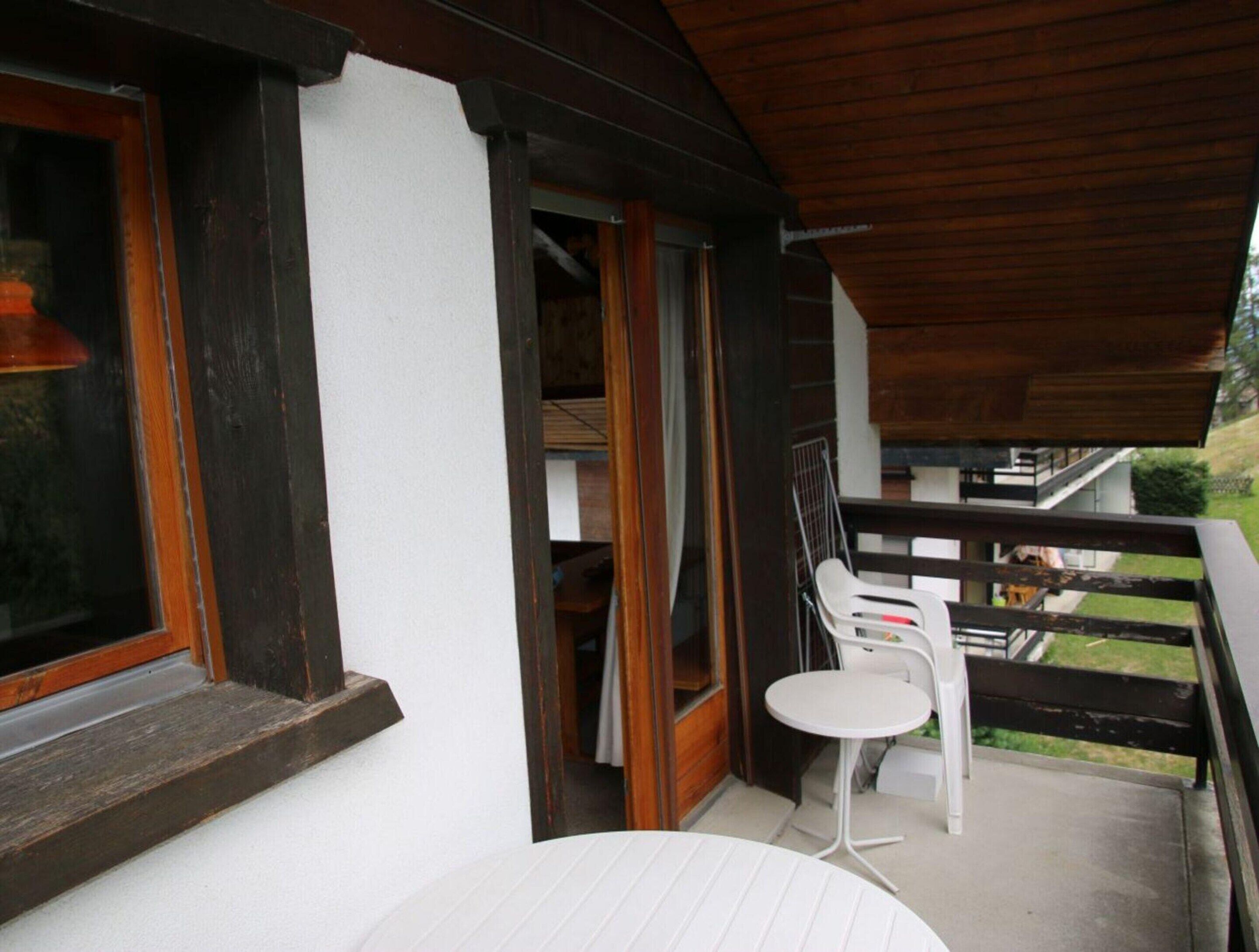 Ein Balkon mit weißem Tisch und Stühlen, Holzgeländern und Blick auf die Umgebung.