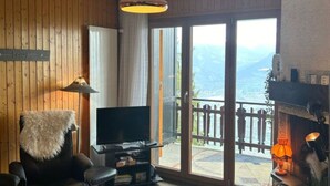 Ein Wohnzimmer mit Fernseher, einem Fellteppich und Blick auf einen Balkon mit Holzbalkon.