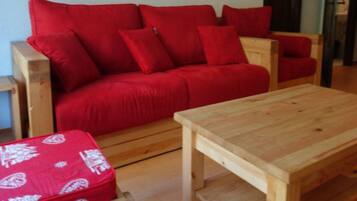 A red sofa with multiple cushions, a wooden coffee table, and a small wooden side table.