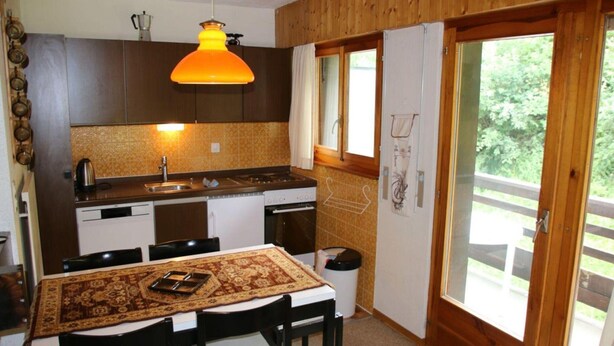 Eine Küche mit Holzausstattung, einem Esstisch mit Stühlen und einem großen Fenster.