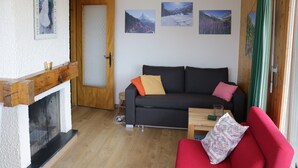 Ein Wohnzimmer mit Kamin, einer Couch, einem roten Sessel und drei gerahmten Bildern an der Wand.
