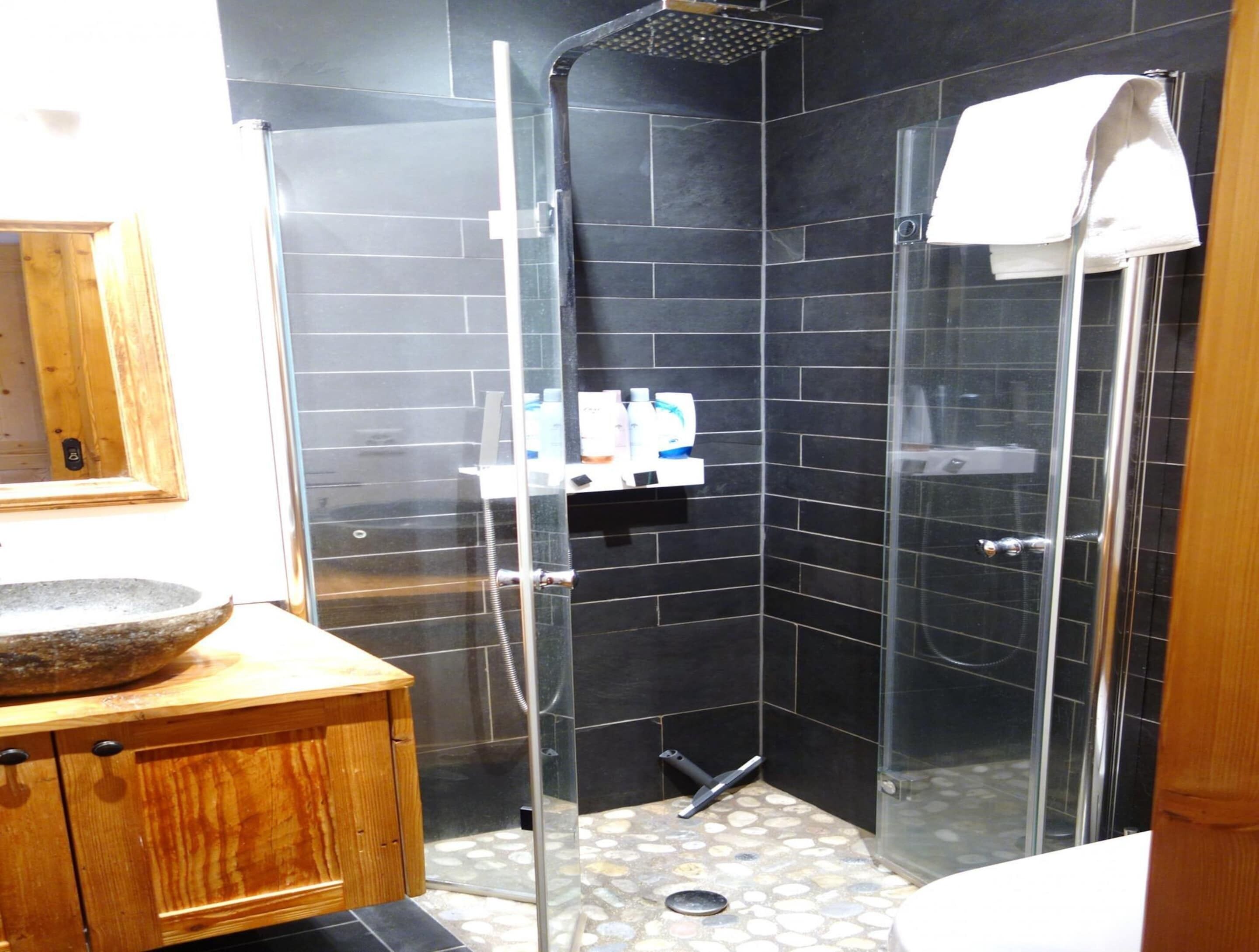 A bathroom with a glass shower enclosure, a wooden vanity, and a stone sink.