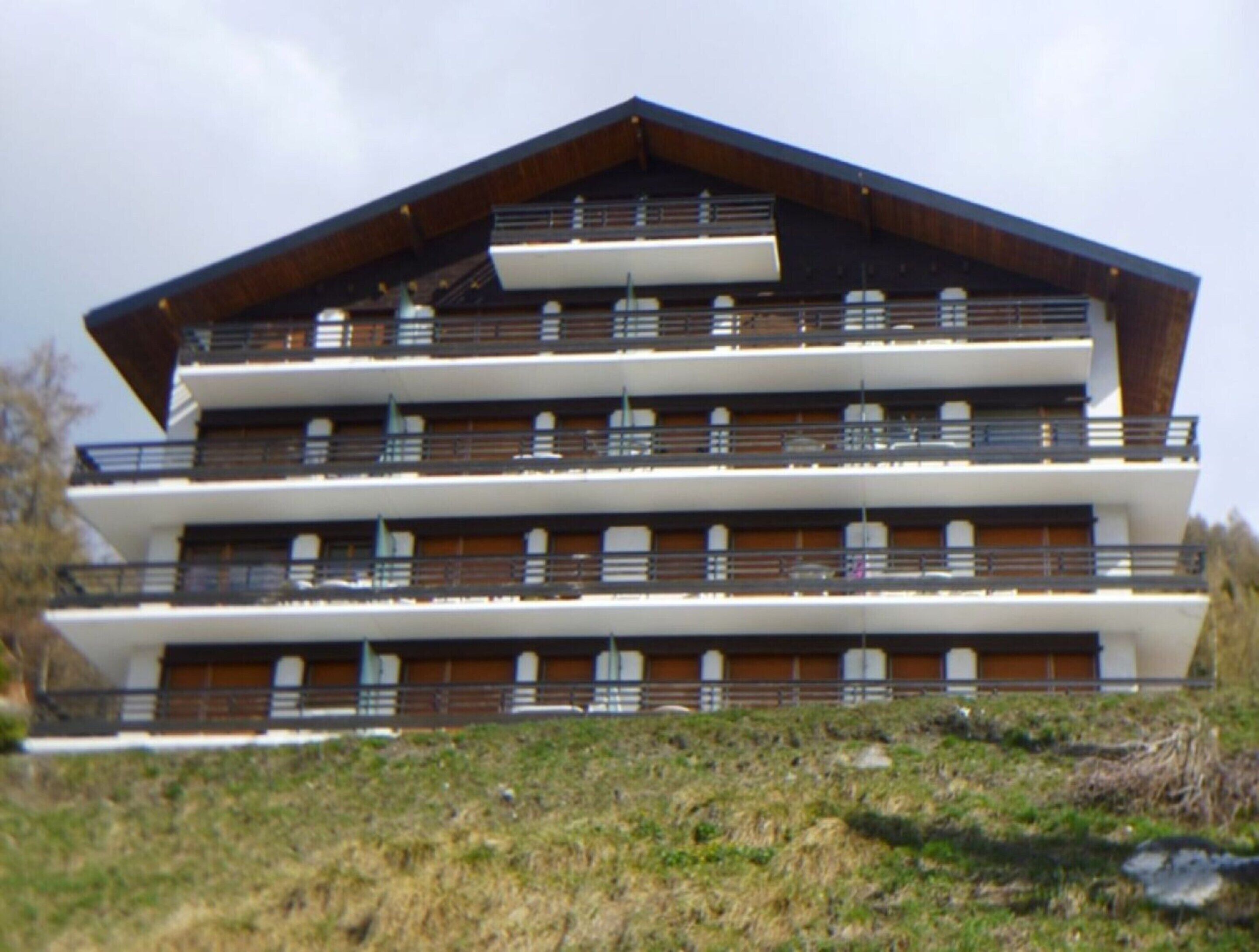 Un immeuble à plusieurs étages, doté de balcons, d’un toit en pente et d’une façade blanche.