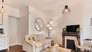 A modern living room with a sofa, a fireplace, a TV, and a dining area. - Cosy Apartment Parc des Expositions/eiffel Tower (Paris)