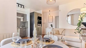 A dining area with a table set for four, a sofa, a mirror, and a kitchen in the background. - Cosy Apartment Parc des Expositions/eiffel Tower (Paris)