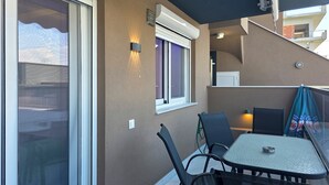 Un balcón con mesa y sillas, una ventana con persianas y un equipo de aire acondicionado.