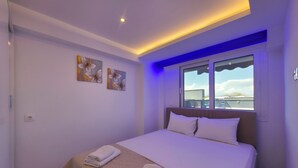 Un dormitorio con cama, dos cuadros en la pared, una ventana con vistas y una lámpara en el techo.