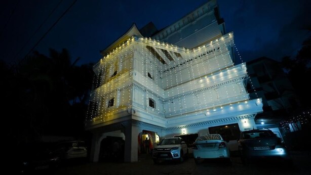 Ein mehrstöckiges Gebäude mit Balkon, beleuchtet durch Lichterketten, mit parkenden Autos davor.