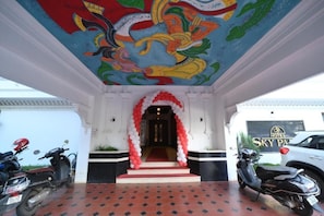A hotel entrance with a colorful mural, a red and white archway, and a red carpet leading to the door.