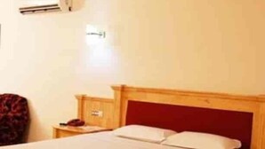 Ein Einzelbett mit Holzrahmen und rotem Kopfteil, ein Nachttisch und eine Wand-Klimaanlage.