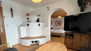 A compact living space with a round wooden table, a sofa, a TV, and a bed in the background. - Apartment Saalfelden 23 (Saalfelden am Steinernen Meer)