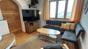 A cozy living room with a wooden floor, a flat-screen TV, a sofa, a bench, and a small table. - Apartment Saalfelden 23 (Saalfelden am Steinernen Meer)
