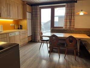 A kitchen with wooden cabinets, a dining table with chairs, and a window with curtains. - Apartment Saalfelden 23 (Saalfelden am Steinernen Meer)