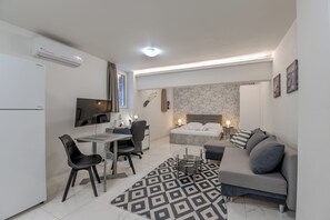 A compact hotel room with a bed, a sofa, a desk with chairs, a TV, and a small table. - Paleo Faliro Gardenbay (Paleo Faliro)