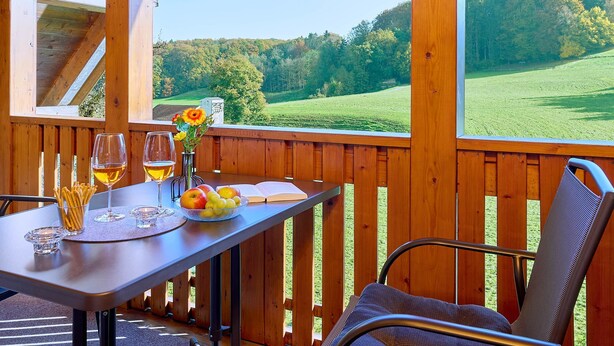 A wooden deck with a table set for two, featuring wine glasses, a bowl of fruit, and a book. - Vacation apartment Sonnenblume, up to 2 persons, top floor, 50 sqm (Waging am See)