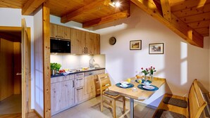 A kitchen with wooden cabinets, a microwave, and a dining area with a table, chairs, and a bench. - Vacation apartment Sonnenblume, up to 2 persons, top floor, 50 sqm (Waging am See)